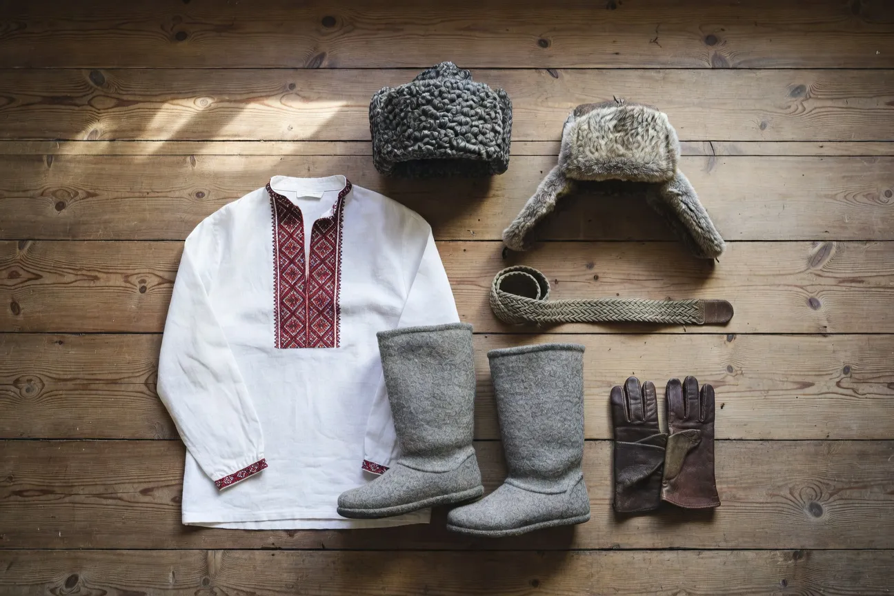 Flat-lay du vestiaire russe homme complet : kosovorotka brodée, valenki gris, papakha, ouchanka, ceinture cosaque, gants