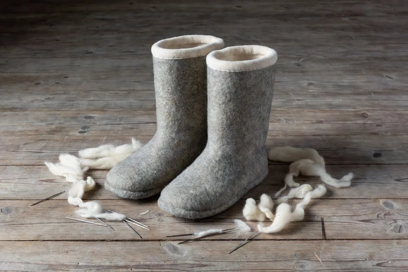 Une paire de valenki traditionnels en feutre gris et crème sur un plancher en bois avec laine brute